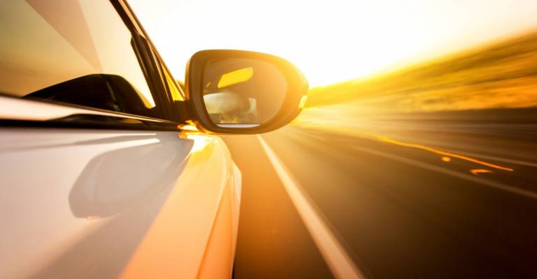 Een close-up van een autospiegel van een auto dat richting de ondergaande zon rijdt