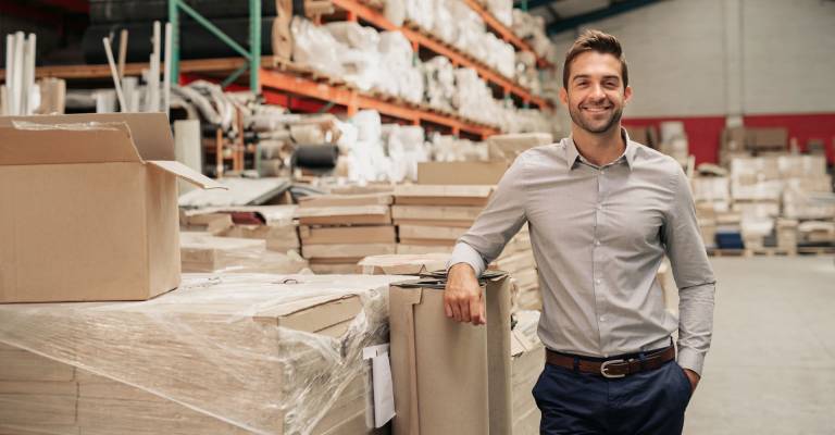 Manager glimlachend terwijl hij tegen de voorraad leunt in een groot magazijn